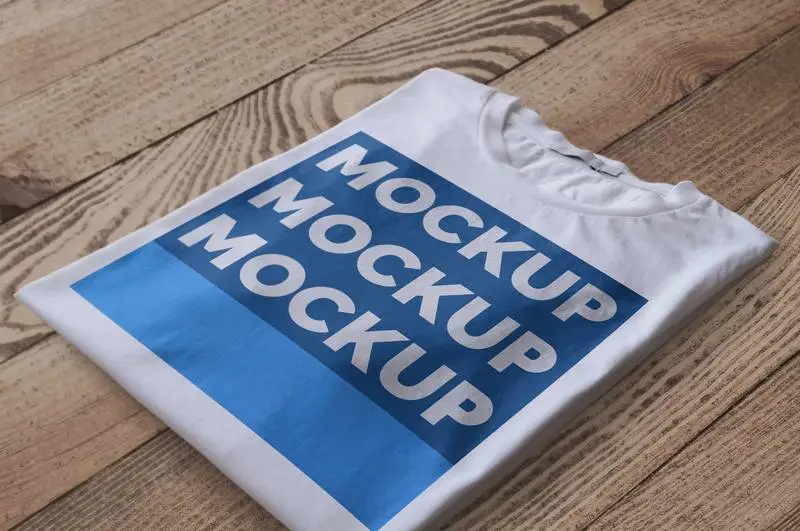 Folded White T-Shirt Over Wood Surface Mockup