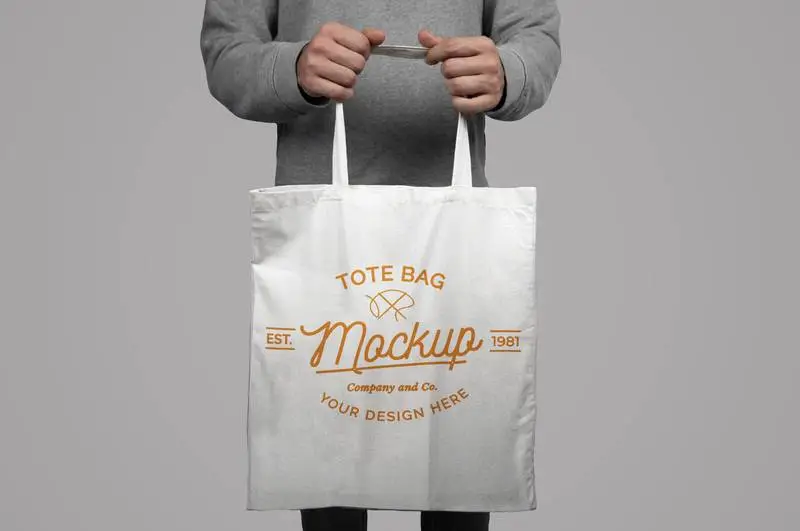 Mockup of Model Holding a Tote Bag on a Gray Background