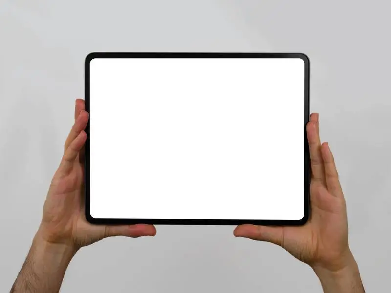White Tablet Pro Screen Horizontally Held by Two Hands on a Light Background