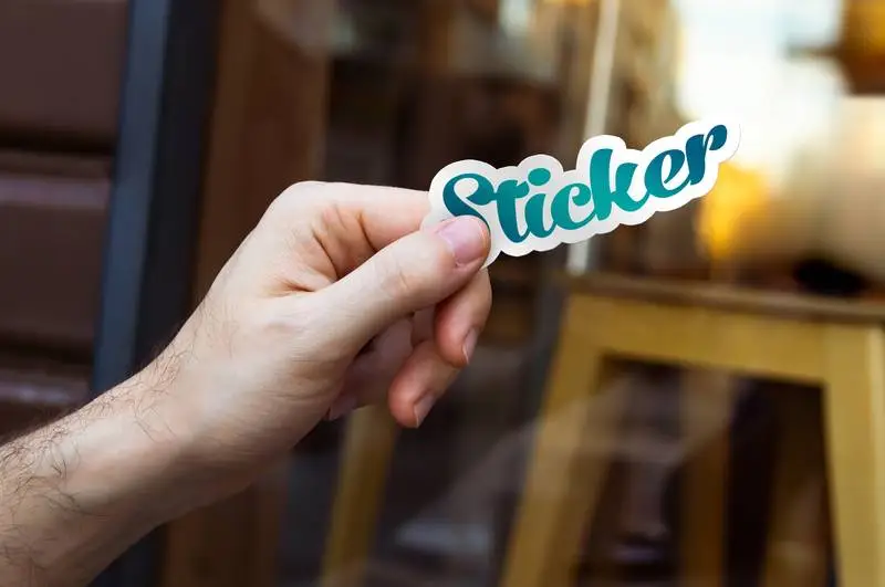 Mockup of Hand Holding a Sticker in Outdoor Scene