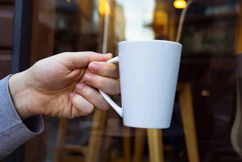 White Mug Held by a Hand on an Outdoor Background