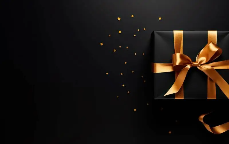 Photo of Gift Box with Black Paper and Gold Ribbon on Dark Background