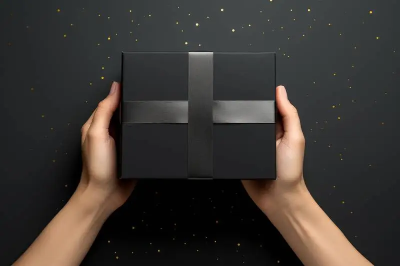 Image of Hand Holding Black Gift Box on Dark Background