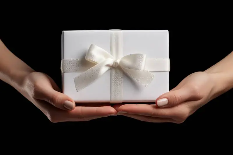Image of Hand Holding White Gift Box With Gold Ribbon on Dark Background