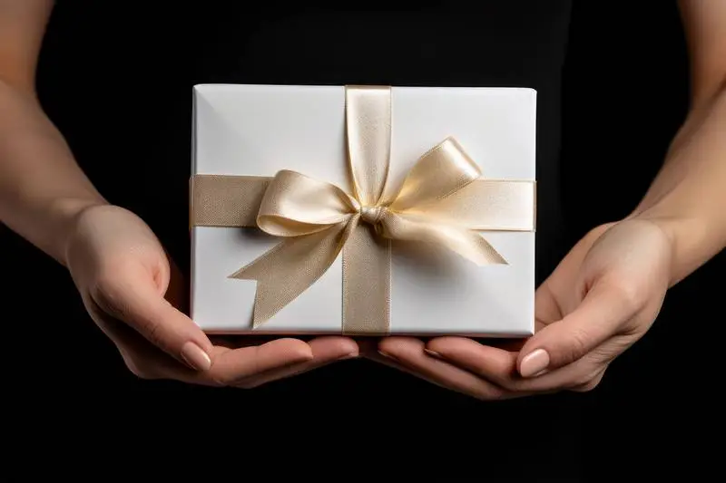 Image of Model Holding White Gift Box With Gold Ribbon on Dark Background