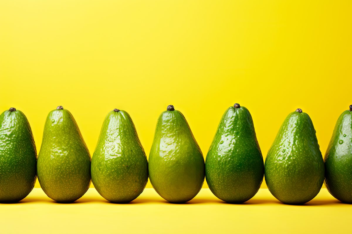 Fresh avocados arranged in a row on a yellow background